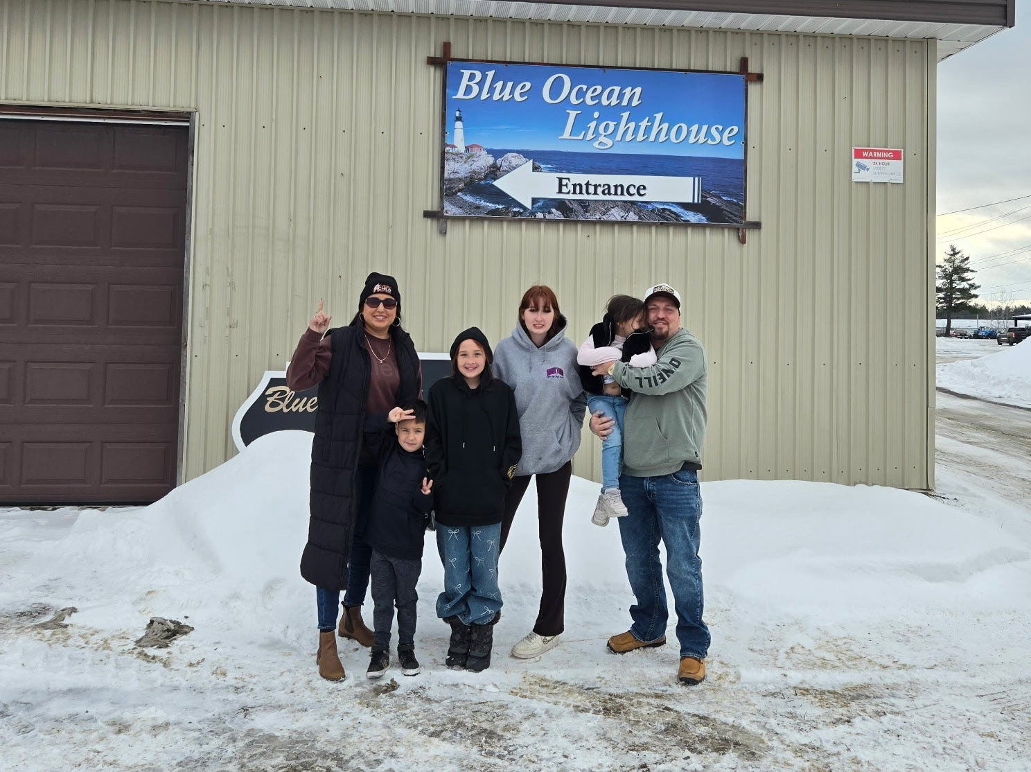 Group of people posing in front of a building with a 'Blue Ocean Lighthouse' sign on a snowy day.